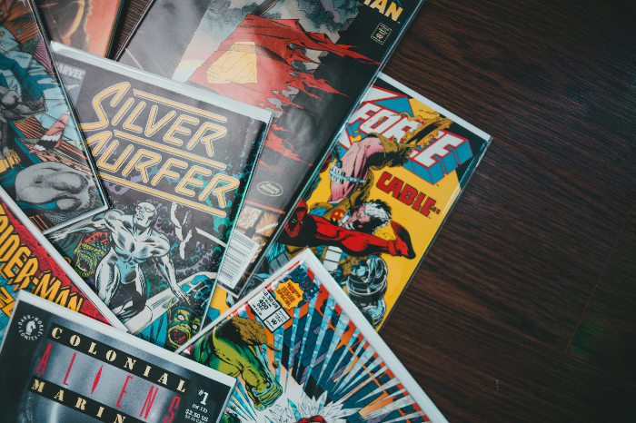 various comic books layed out on top of each other on a dark brown wooden table